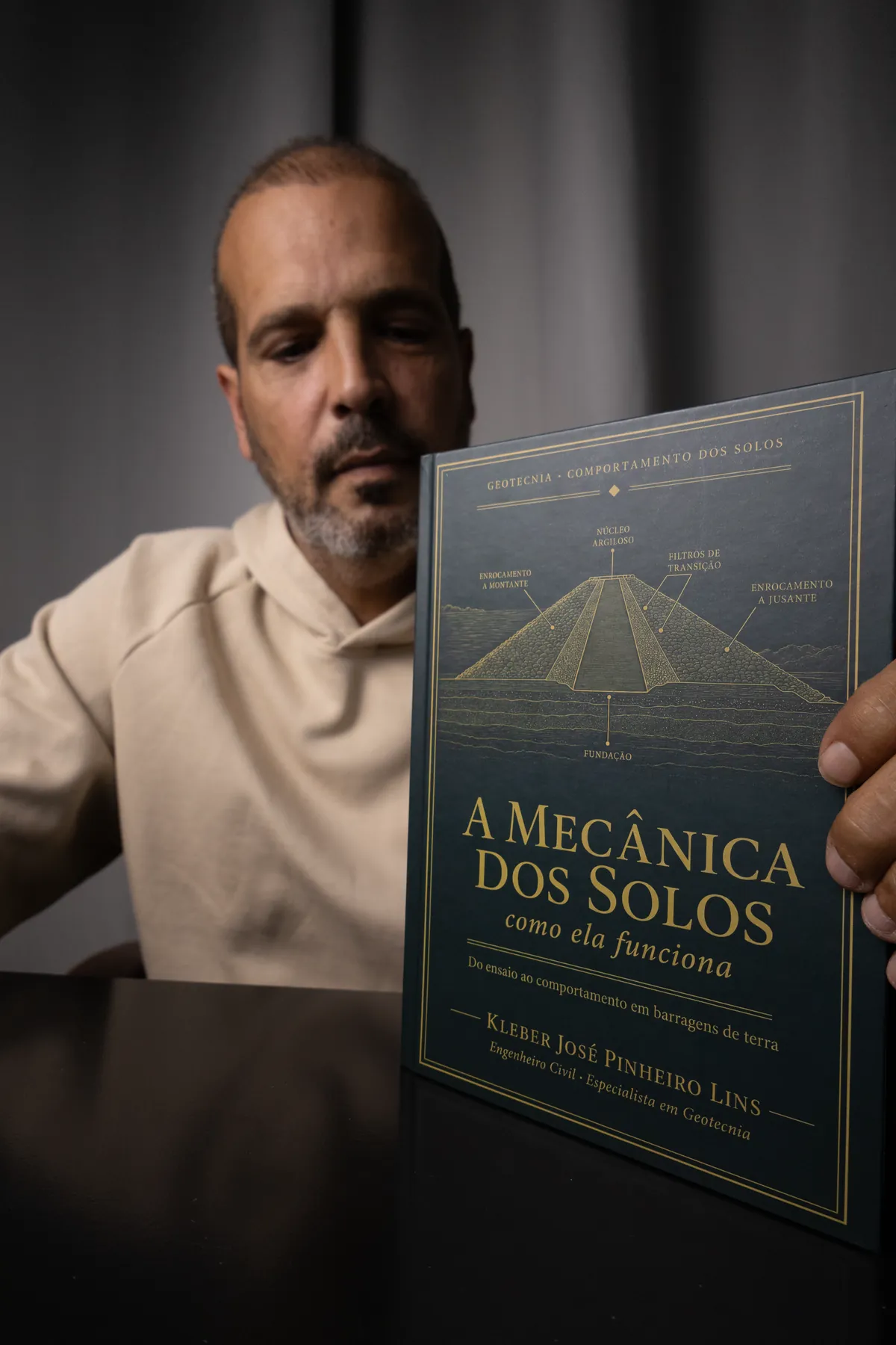 O autor erguendo o livro em direção à câmera, com a capa em foco e o rosto suave ao fundo