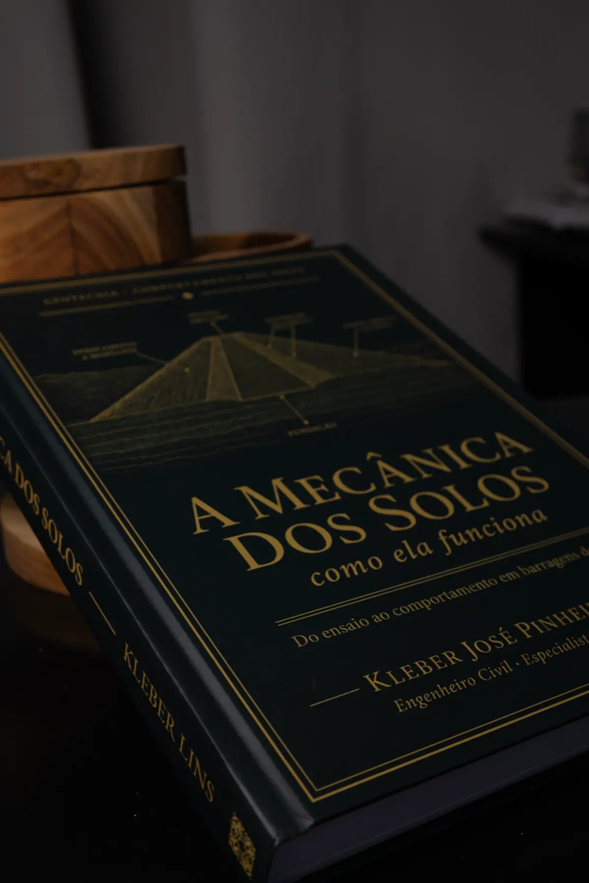 Livro em três quartos sobre a mesa de trabalho, com uma caixa de madeira ao fundo