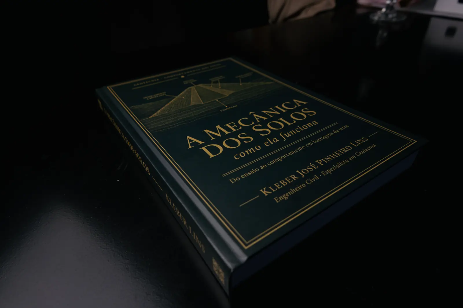 Livro de capa verde-escura deitado numa mesa escura, com luz rasante vinda da esquerda