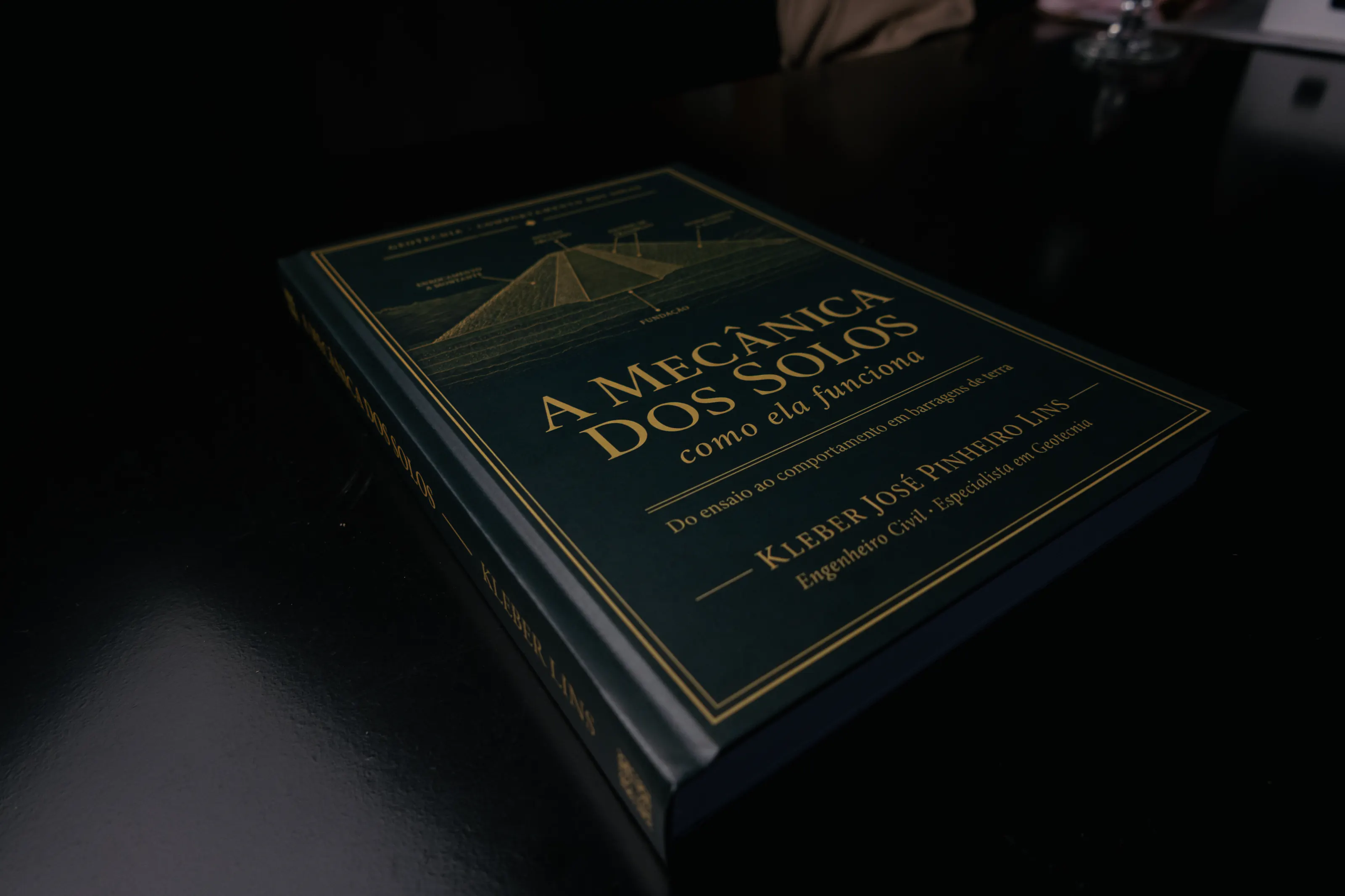 Livro de capa verde-escura deitado numa mesa escura, com luz rasante vinda da esquerda