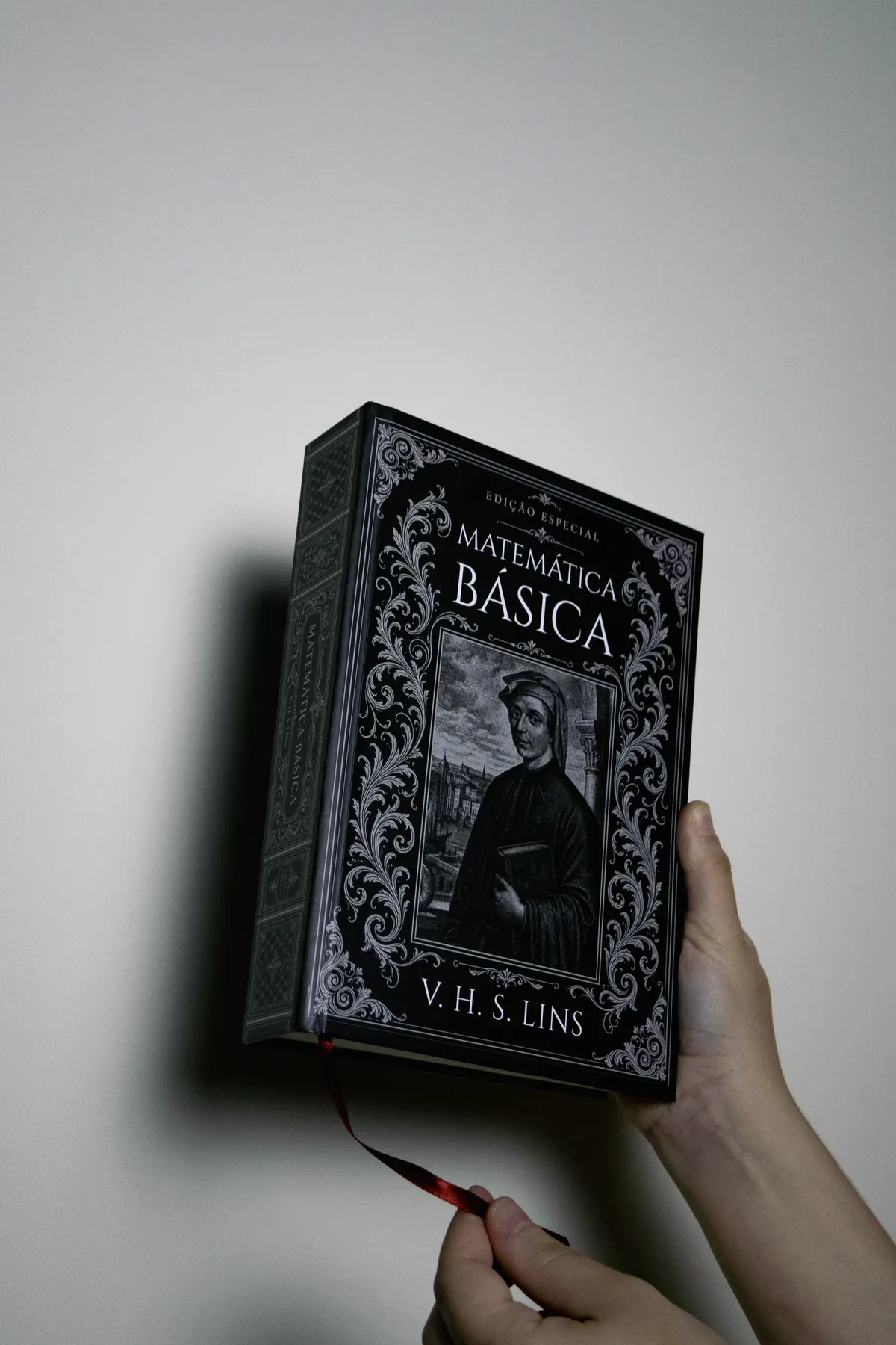 Livro segurado na mão contra fundo claro de estúdio, com a fita marcadora à mostra