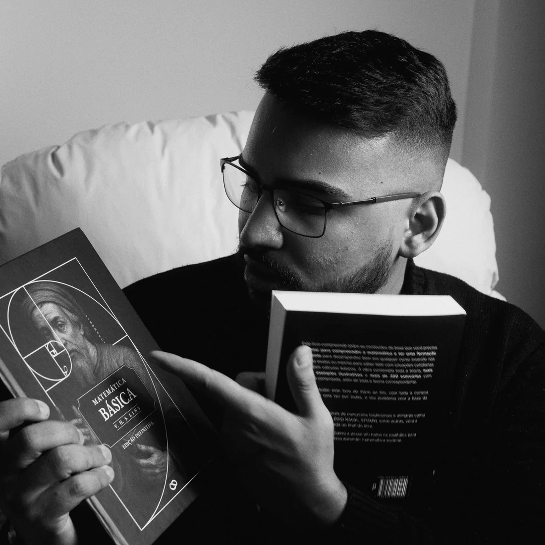Retrato em preto e branco de Victor Lins lendo, com dois exemplares de Matemática Básica nas mãos